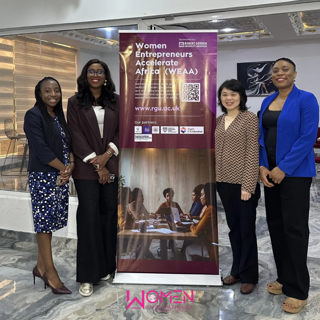 A group of women standing by an event roll up stand banner at an event entrance.