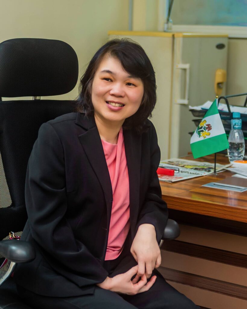 A white Asian female wearing a black jacket and seated in an office facing the left side of the photo