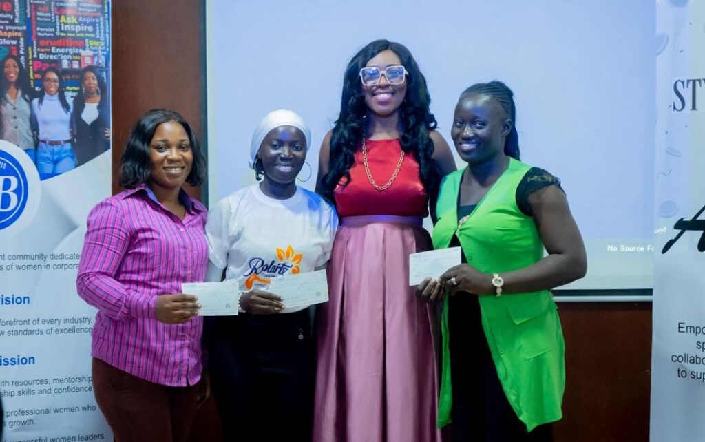 4 black women at an event, standing in front of the event banner in a room and smiling to the camera